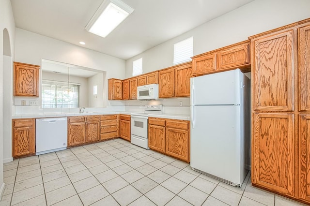 kitchen with light countertops, light tile patterned floors, brown cabinetry, white appliances, and a sink