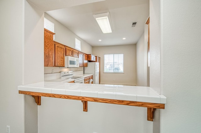 kitchen featuring white appliances, visible vents, light countertops, a kitchen bar, and brown cabinets