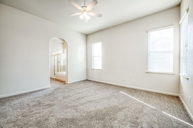 carpeted empty room featuring baseboards, arched walkways, and ceiling fan