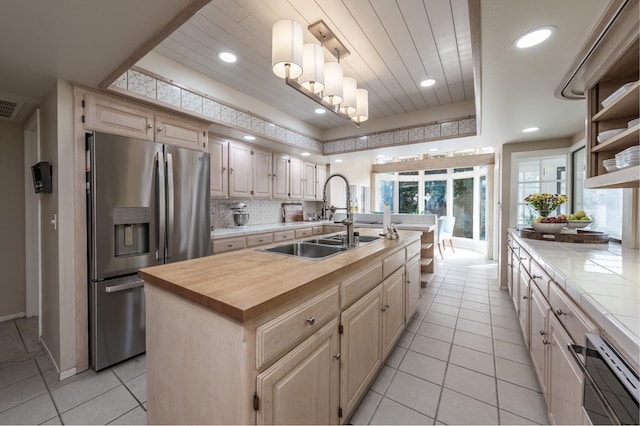 kitchen featuring a kitchen island with sink, a sink, open shelves, tasteful backsplash, and stainless steel fridge with ice dispenser