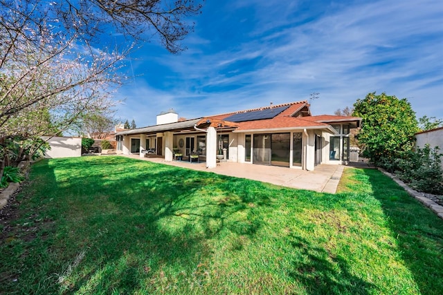 rear view of property with solar panels, a chimney, a yard, a sunroom, and a patio area