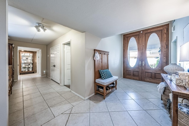 foyer with light tile patterned flooring, french doors, baseboards, and a textured ceiling