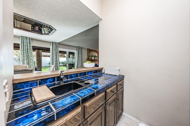 bar featuring a sink, baseboards, a textured ceiling, and light tile patterned flooring