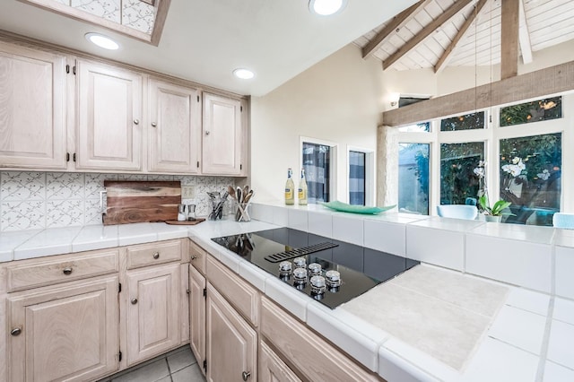 kitchen with decorative backsplash, tile countertops, light tile patterned flooring, black electric cooktop, and vaulted ceiling with beams