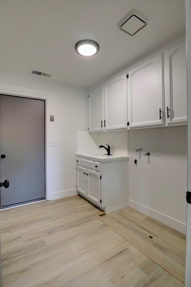 washroom with light wood-style flooring, cabinet space, visible vents, and baseboards