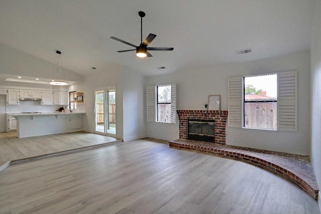 unfurnished living room with a ceiling fan, visible vents, lofted ceiling, a brick fireplace, and light wood-type flooring