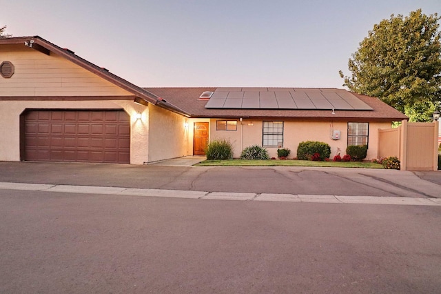 view of front of home with solar panels, fence, a garage, and stucco siding