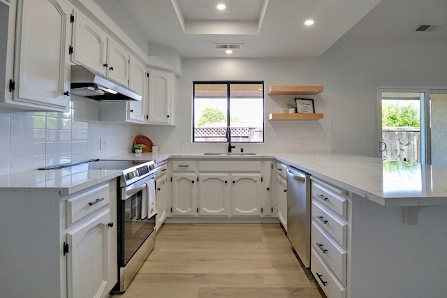 kitchen featuring visible vents, a peninsula, stainless steel appliances, under cabinet range hood, and white cabinetry