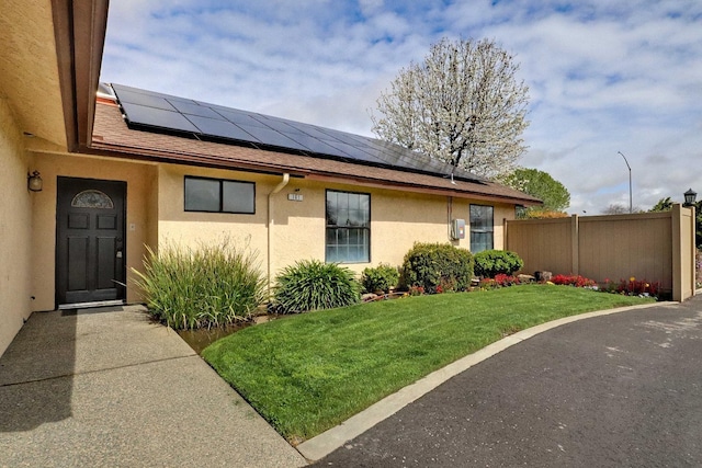 view of exterior entry with solar panels, a yard, fence, and stucco siding