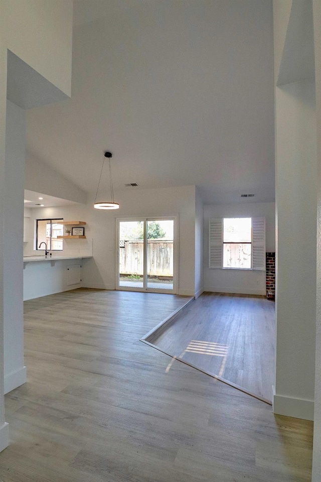 unfurnished living room with a sink, visible vents, baseboards, and wood finished floors