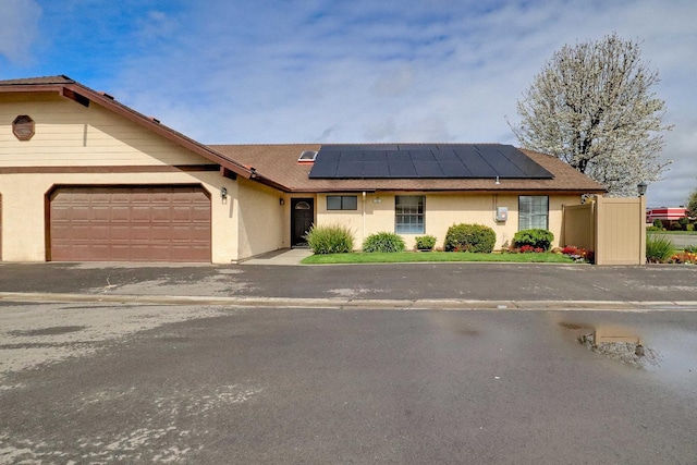 ranch-style house with stucco siding, solar panels, an attached garage, and fence