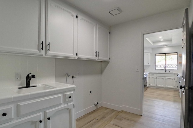 washroom featuring cabinet space, electric dryer hookup, light wood-style floors, and a sink