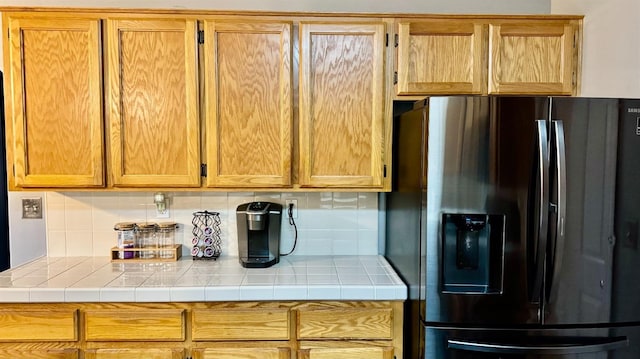 kitchen featuring tile countertops, backsplash, and black refrigerator with ice dispenser