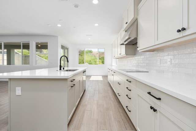 kitchen featuring recessed lighting, under cabinet range hood, a sink, a kitchen island with sink, and tasteful backsplash