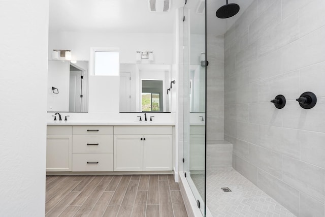 full bath featuring a sink, double vanity, tiled shower, visible vents, and wood finished floors