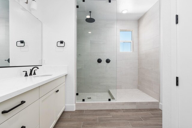 bathroom featuring baseboards, wood finish floors, vanity, and tiled shower
