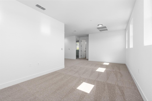 empty room featuring light carpet, visible vents, and baseboards
