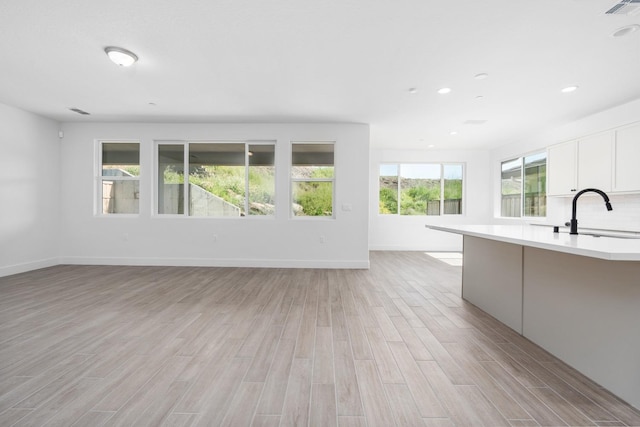 unfurnished living room with light wood-style flooring, visible vents, baseboards, and a sink