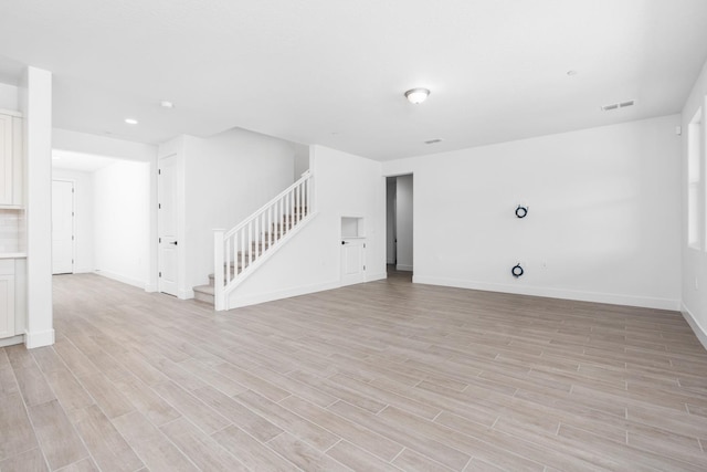 unfurnished room featuring baseboards, stairs, visible vents, and light wood-style flooring