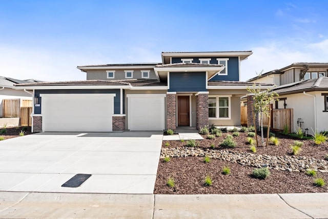 prairie-style house with solar panels, concrete driveway, fence, a garage, and brick siding