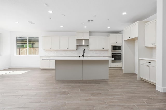 kitchen with a sink, stainless steel appliances, light wood-style flooring, backsplash, and visible vents