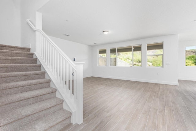 unfurnished living room featuring light wood-style floors, stairway, and baseboards