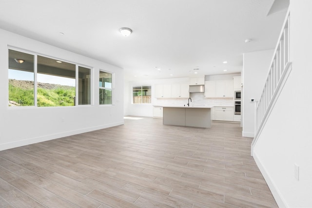 unfurnished living room with baseboards, a sink, and light wood-type flooring