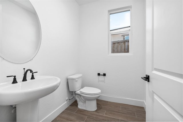 bathroom featuring wood finished floors, toilet, baseboards, and a sink