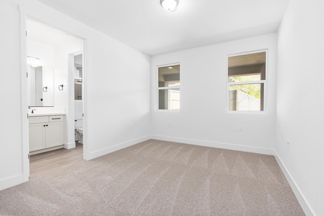 unfurnished bedroom with light colored carpet, baseboards, ensuite bathroom, and a sink