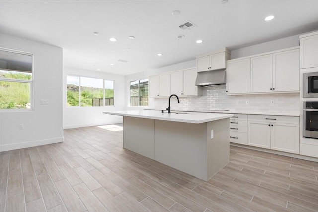 kitchen with a sink, decorative backsplash, appliances with stainless steel finishes, under cabinet range hood, and visible vents
