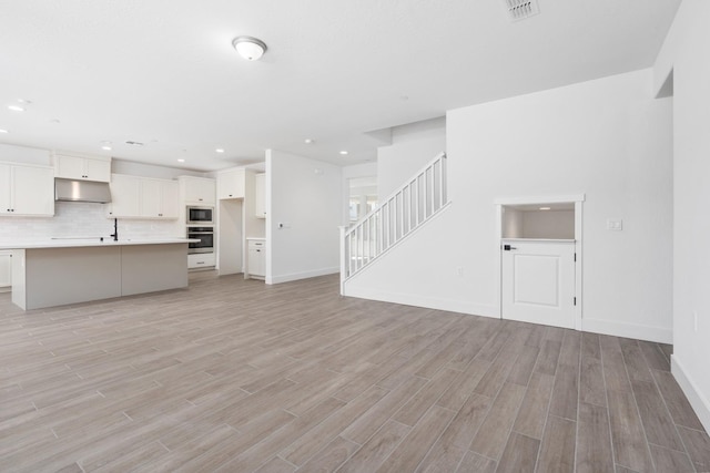 unfurnished living room featuring stairway, light wood finished floors, baseboards, visible vents, and recessed lighting