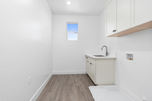 laundry room featuring hookup for a washing machine, a sink, cabinet space, dark wood finished floors, and baseboards