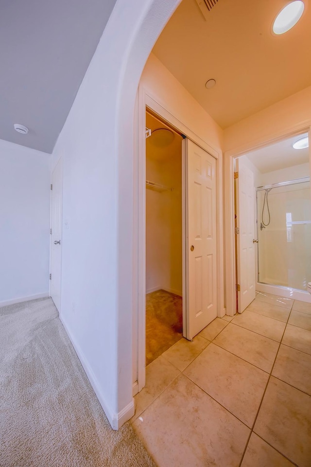 corridor featuring light tile patterned floors, baseboards, arched walkways, and light colored carpet