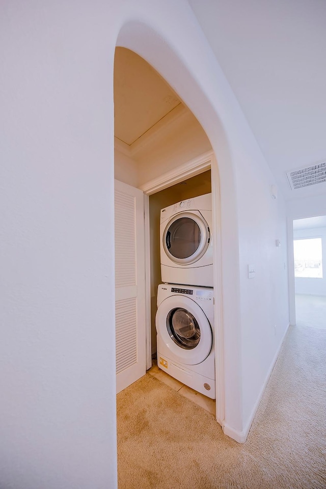 washroom with baseboards, visible vents, laundry area, stacked washer / drying machine, and light carpet