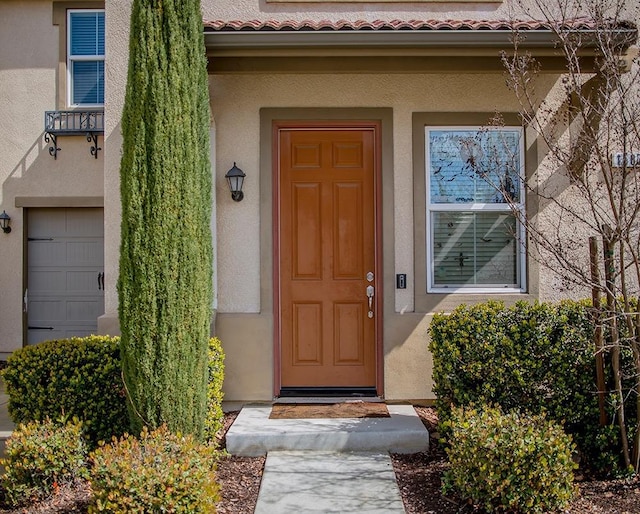 property entrance featuring stucco siding, a garage, and a tiled roof