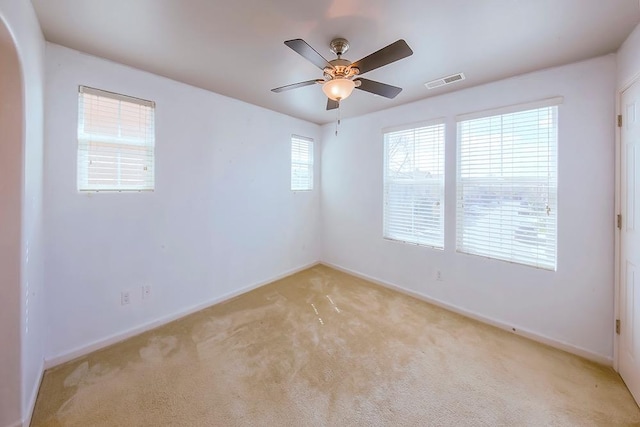 empty room with visible vents, baseboards, light colored carpet, arched walkways, and a ceiling fan