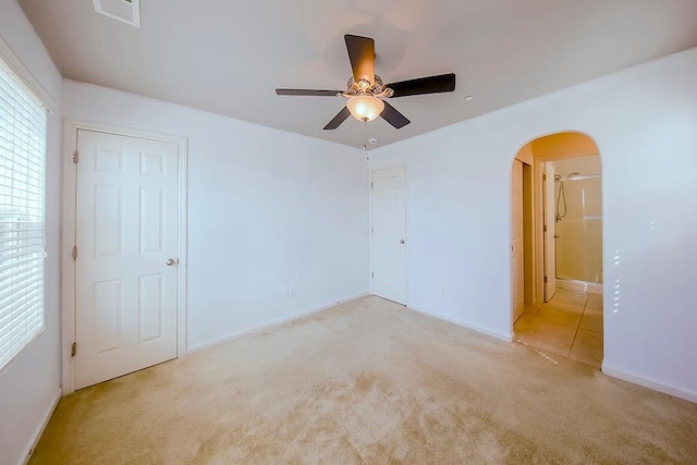 carpeted spare room featuring arched walkways, visible vents, baseboards, and ceiling fan