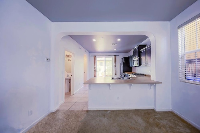 kitchen with stainless steel microwave, a kitchen breakfast bar, a peninsula, arched walkways, and a sink