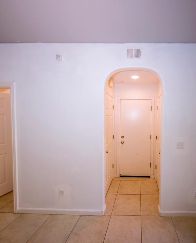 hall featuring visible vents, arched walkways, baseboards, and light tile patterned flooring