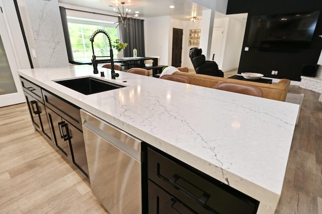 kitchen featuring stainless steel dishwasher, light wood-style floors, an inviting chandelier, and a sink