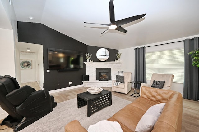 living area with vaulted ceiling, light wood-style flooring, a fireplace, and ceiling fan