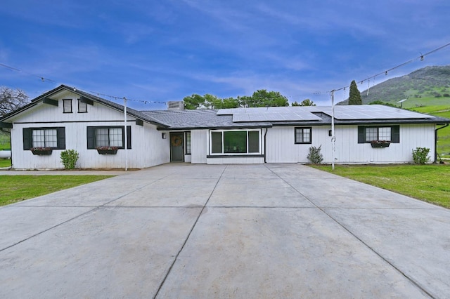 ranch-style home with concrete driveway, a front lawn, and solar panels