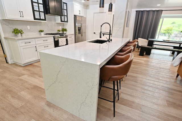 kitchen featuring a sink, appliances with stainless steel finishes, a kitchen breakfast bar, light wood-style floors, and light stone counters