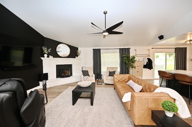 living area featuring vaulted ceiling, wood finished floors, a fireplace, and ceiling fan
