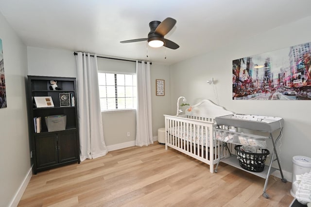 bedroom featuring baseboards, a ceiling fan, a crib, and wood finished floors
