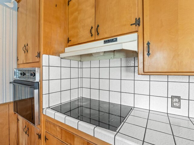 9414 E Belmont Ave, Sanger, CA 93657 - kitchen with wall oven, tile counters, under cabinet range hood, black electric cooktop, and tasteful backsplash