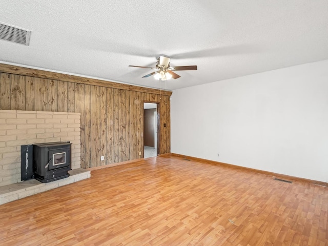 9414 E Belmont Ave, Sanger, CA 93657 - unfurnished living room featuring ceiling fan, wood finished floors, wooden walls, a wood stove, and a textured ceiling