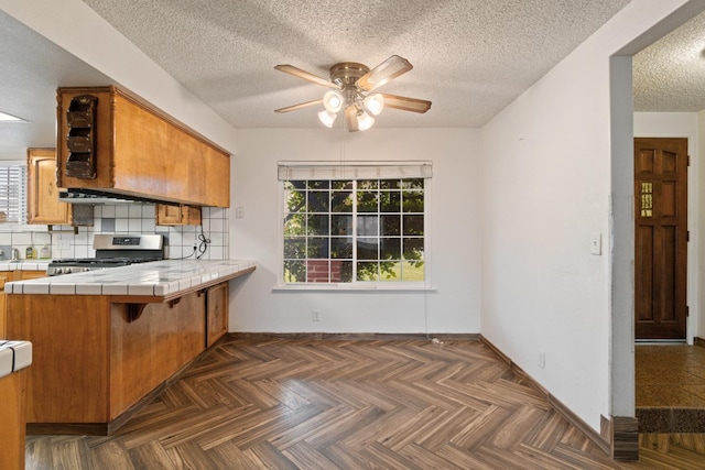 210 S Caesar Ave, Fresno, CA 93727 - kitchen featuring stainless steel range with gas cooktop, tile counters, a ceiling fan, healthy amount of natural light, and a textured ceiling
