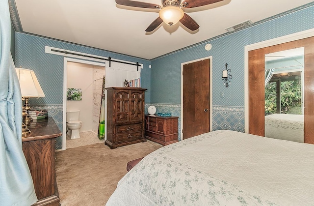 carpeted bedroom with visible vents, wallpapered walls, ceiling fan, ensuite bathroom, and a barn door