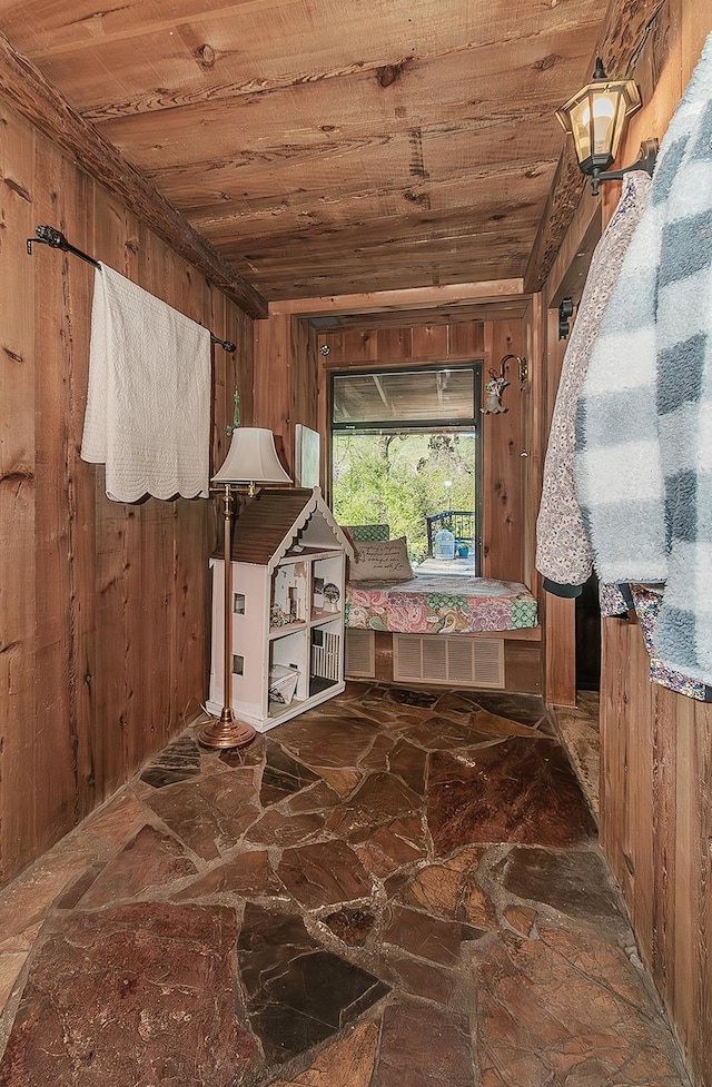 interior space featuring wooden walls, stone floors, wood ceiling, and visible vents